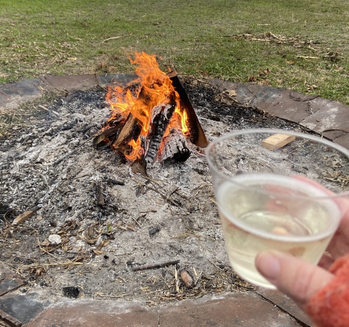 outdoor fire pit with fire burning and a plastic glass of champagne being held up to toast